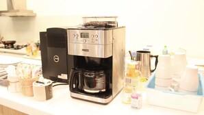 Una cafetera con pantalla digital, una tetera y varios utensilios de cocina sobre una encimera.