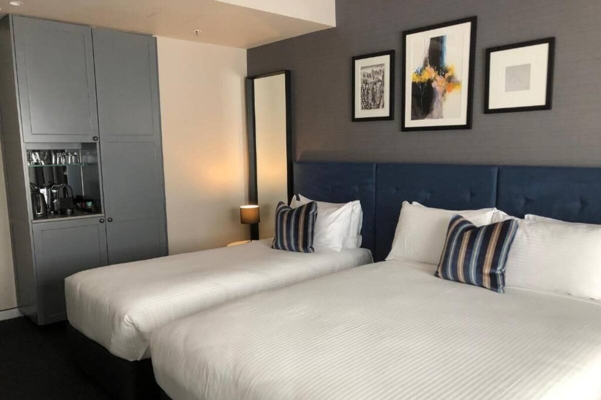 Een hotelkamer met twee bedden, een minibar en kunstwerken in lijsten aan de muur.