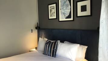 A neatly made bed with white linens and striped pillows, a dark headboard, and three framed artworks on the wall.