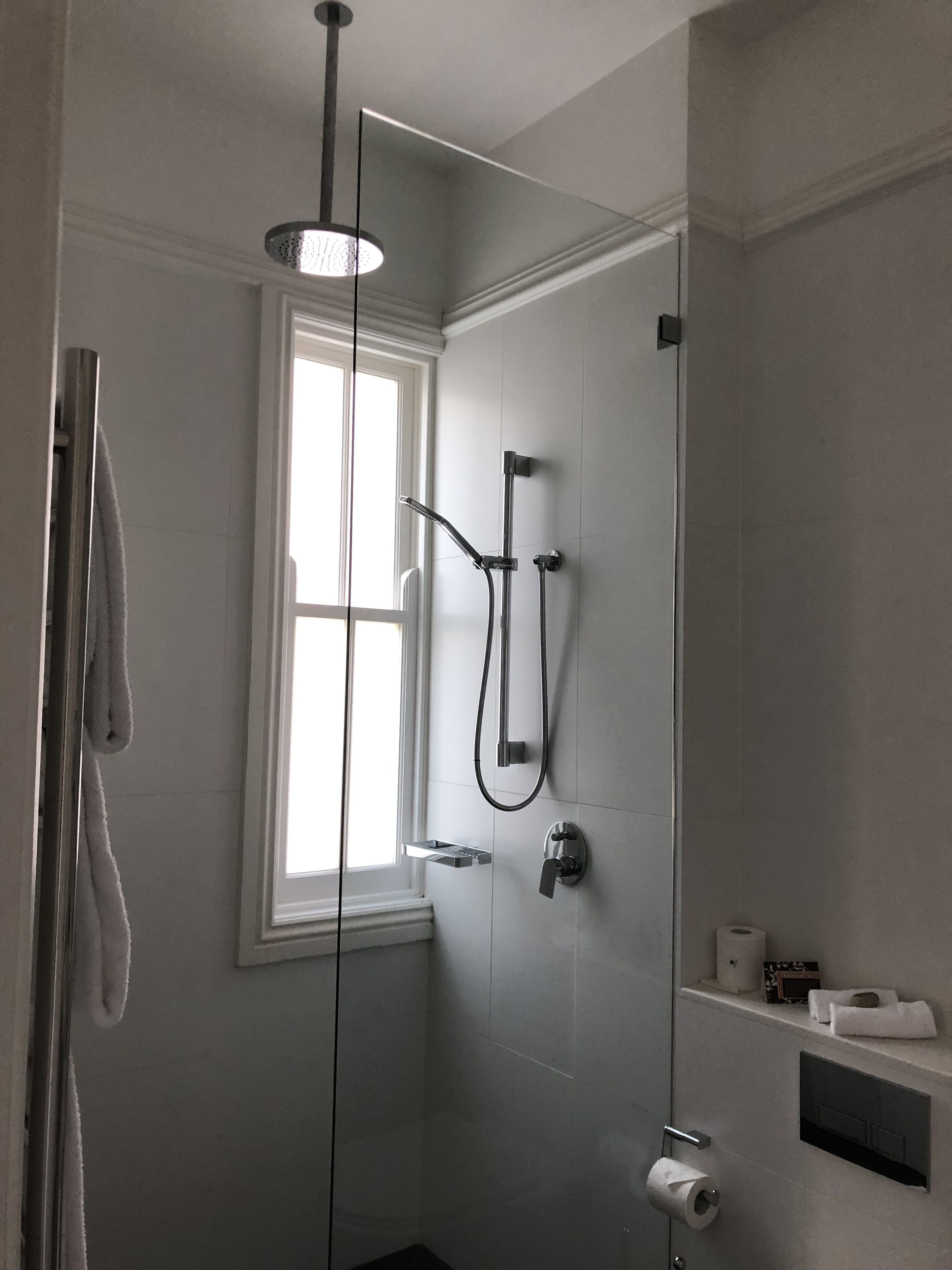 A modern bathroom with a walk-in shower, a window, and a toilet paper holder.