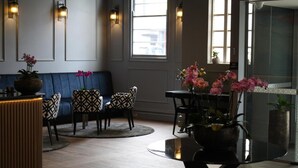 Ein modernes Interieur mit einem blauen Sofa, gemusterten Sesseln, einem runden Tisch und Topfpflanzen.