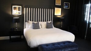 Ein modernes Hotelzimmer mit einem großen Bett, zwei Nachttischen, einem Beistelltisch und einem dunkel gefärbten Ottomanen.