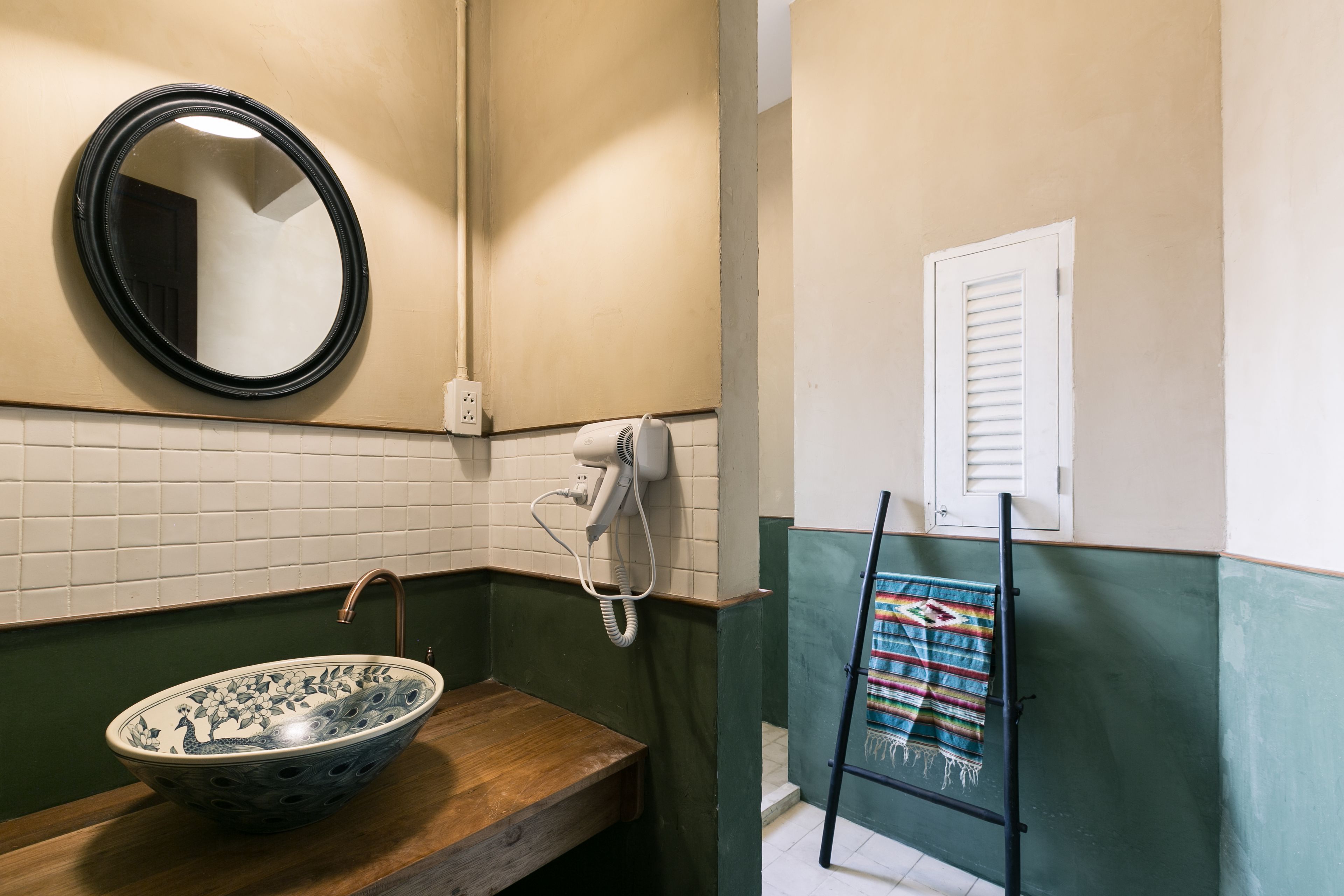 A bathroom with a wooden vanity, a round mirror, a hairdryer, and a colorful towel rack.