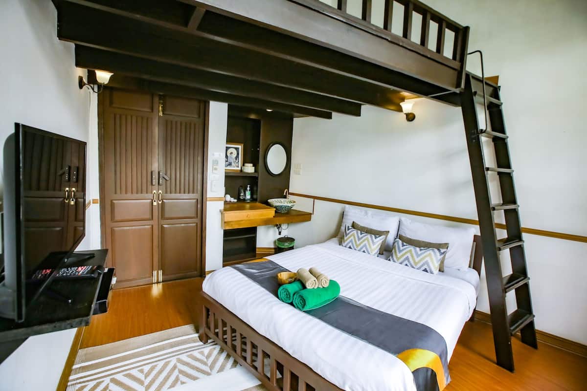 A bedroom with a bunk bed, a desk with a computer, a wooden ladder, and a wardrobe.