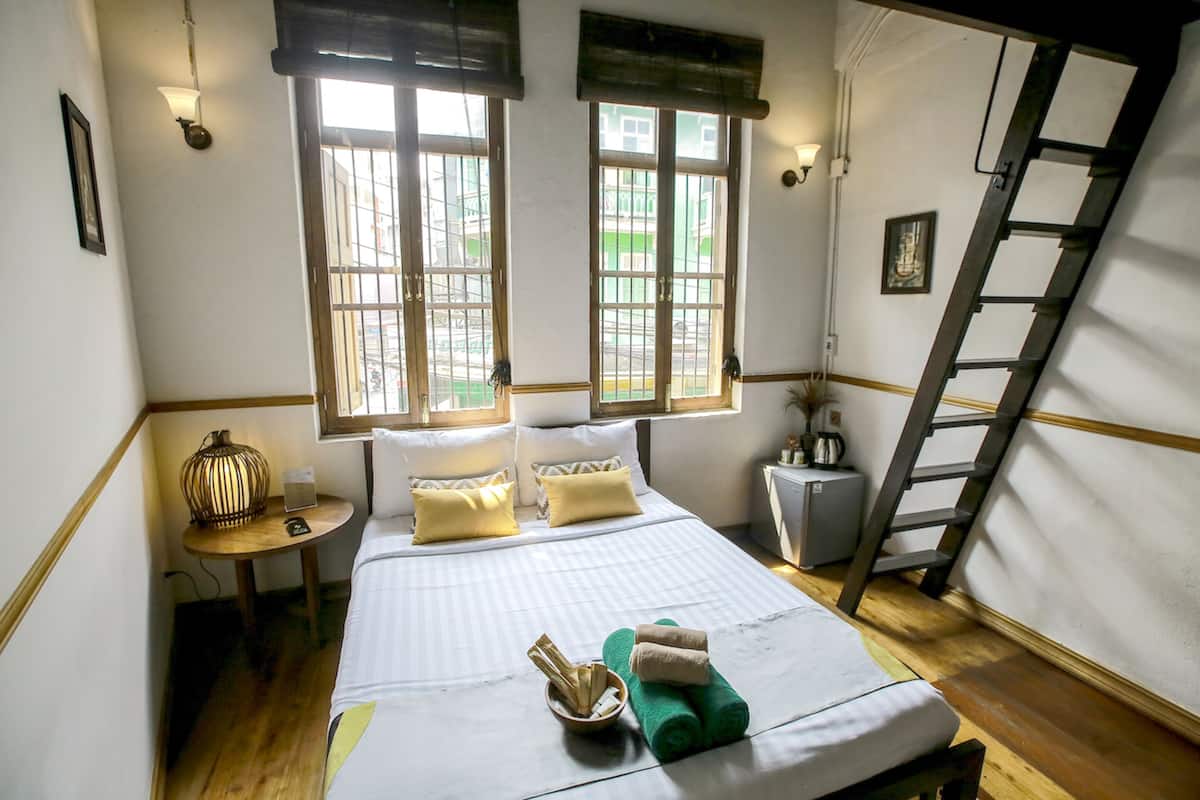 A neatly made bed with pillows, a bedside table with a lamp, and a window with a view of the outside.
