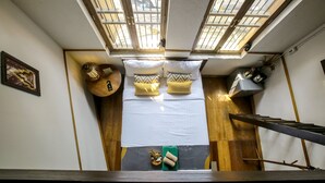 A room with a bed, a small table, and a window with a view of the outside. - 103 - Bed and Brews (Bangkok)
