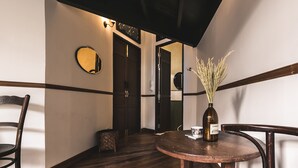 A wooden-floored hallway with a round table and chairs, a vase with dried plants, and a mirror on the wall. - 103 - Bed and Brews (Bangkok)