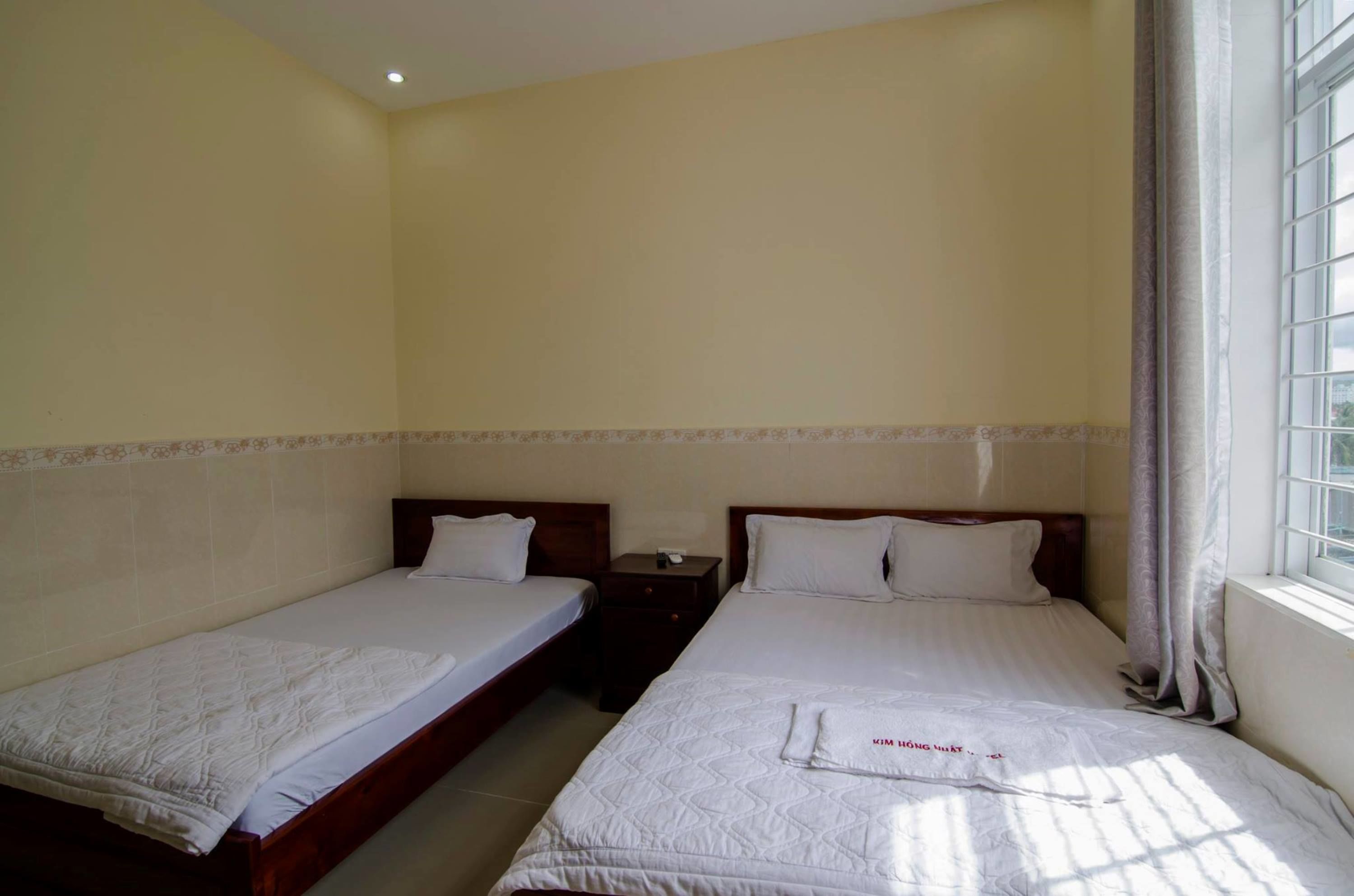 Une chambre d’hôtel avec deux lits simples, une table de chevet et une fenêtre avec des rideaux.
