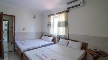 Ein Hotelzimmer mit zwei Einzelbetten, einem hölzernen Kopfteil, einem kleinen Tisch mit Fernbedienung und einer Klimaanlage an der Wand.
