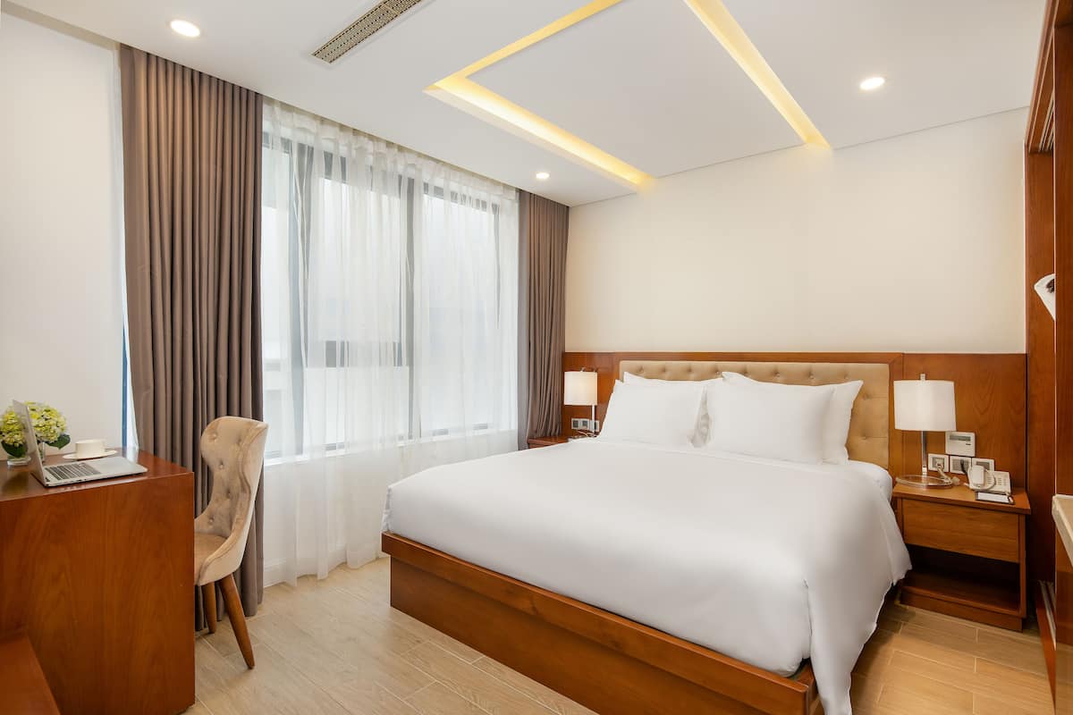 Une chambre d’hôtel avec un grand lit, un bureau avec un ordinateur portable, une chaise et une table de chevet avec une lampe et un téléphone.