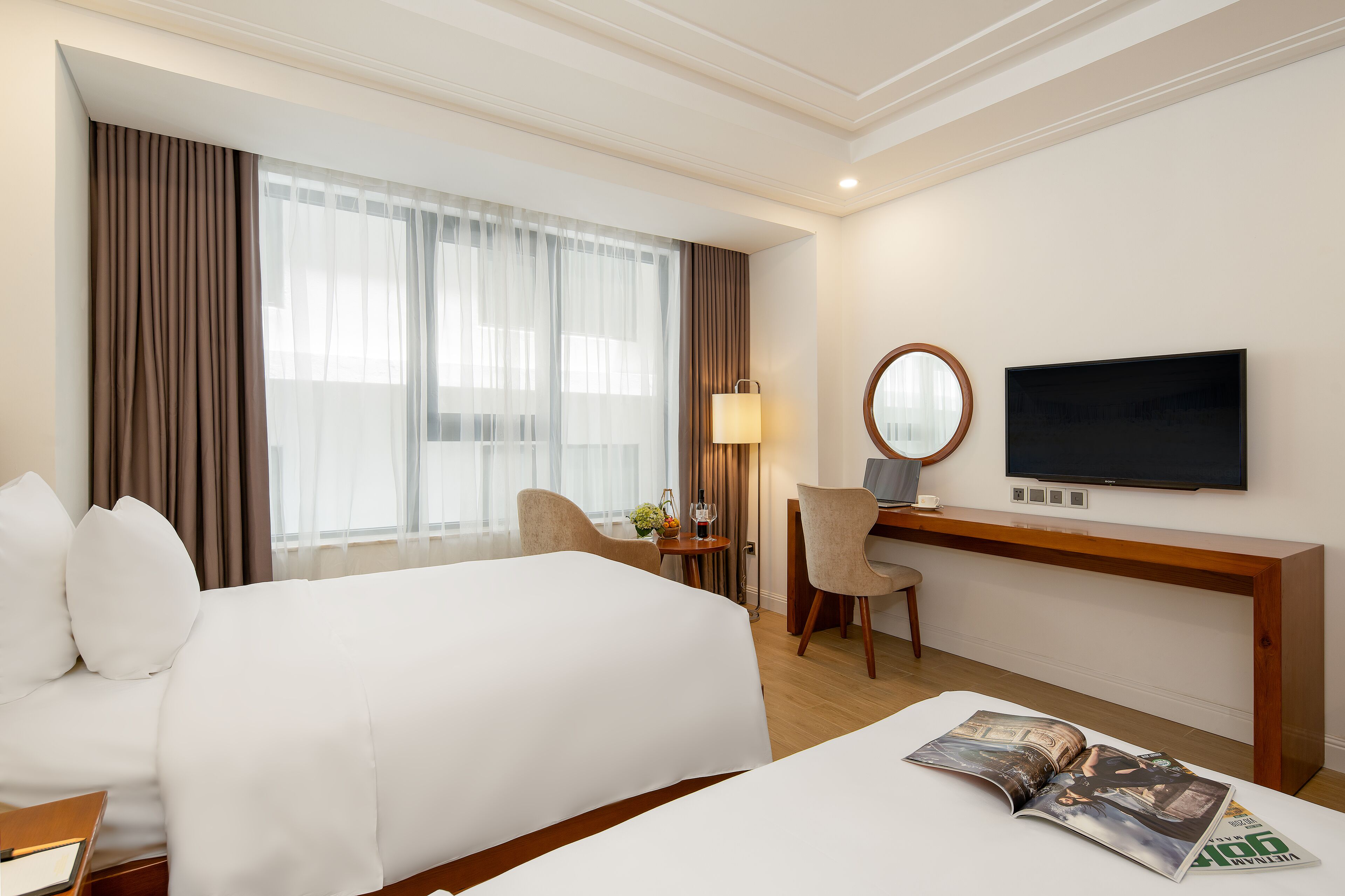 A hotel room with a large bed, a desk with a lamp, a television, and a magazine on the bed.