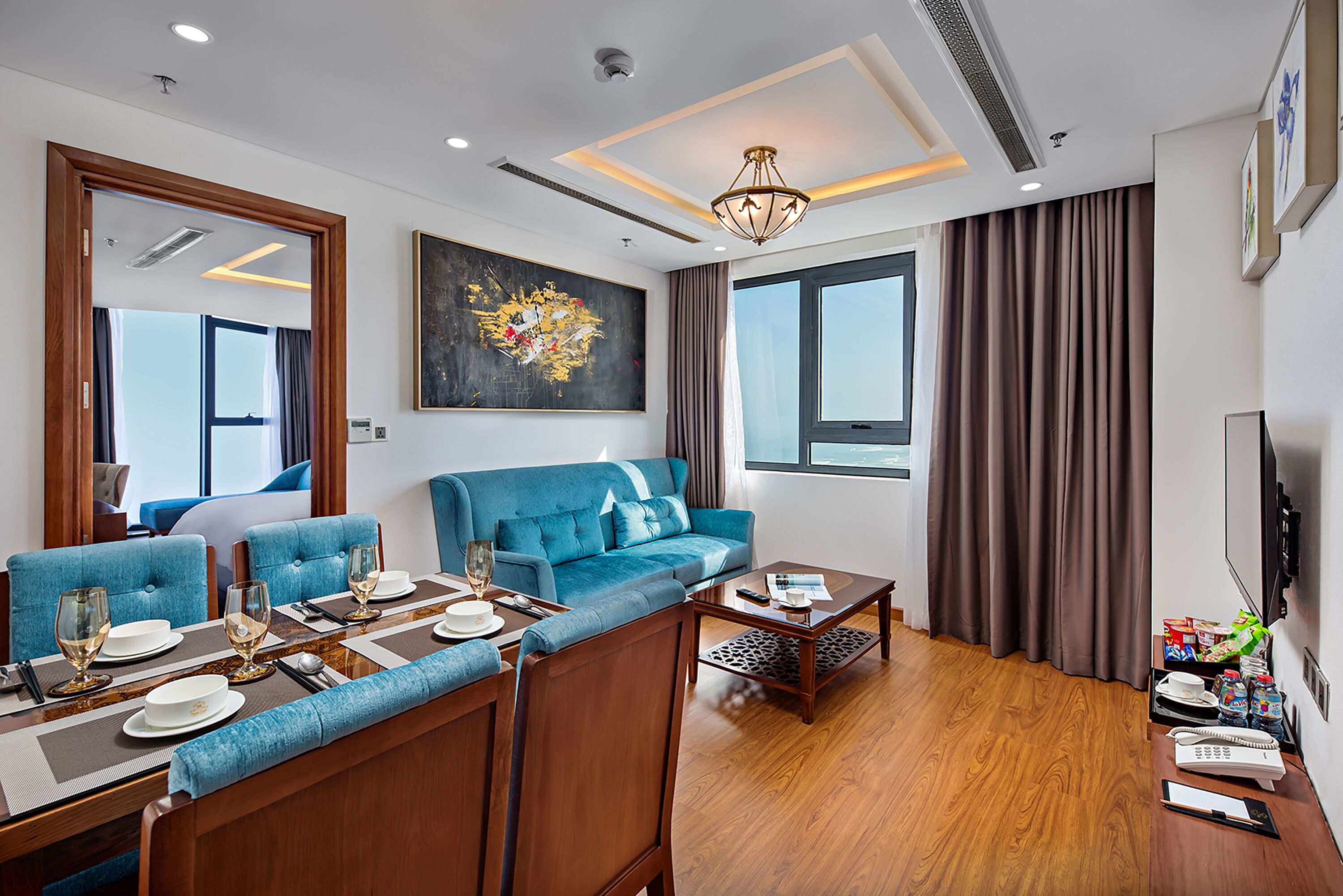 Een moderne woonkamer met een blauwe bank, een eettafelset en een groot raam met gordijnen.