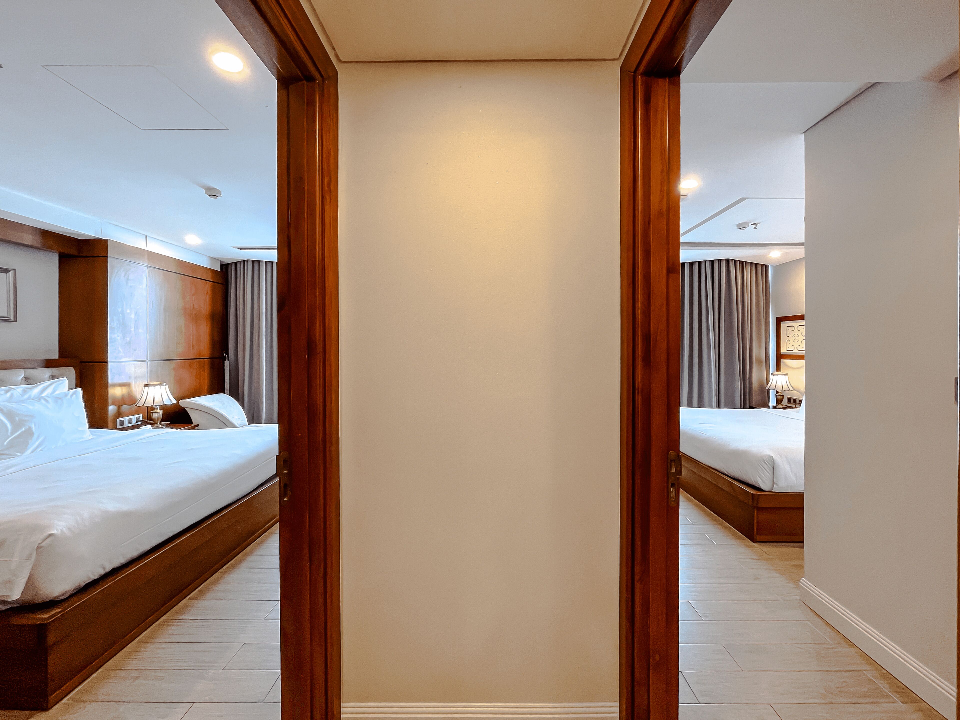 A hotel room with two beds, a wooden wardrobe, and a mirror reflecting the room.