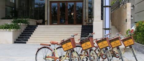 A hotel entrance with a glass facade, a set of stairs leading up to the doors, and four bicycles with signs indicating they are for hotel use.