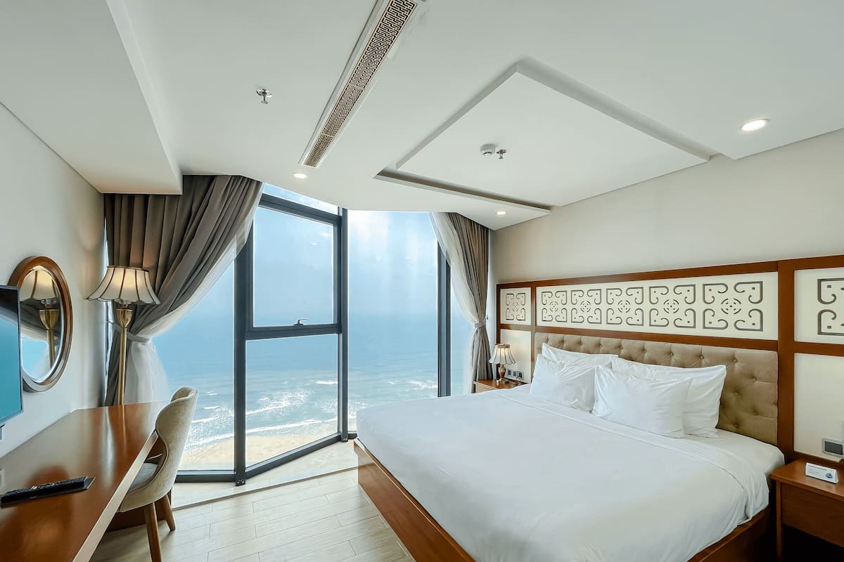 Une chambre d’hôtel avec un grand lit, un bureau, une chaise et une vue sur l’océan.