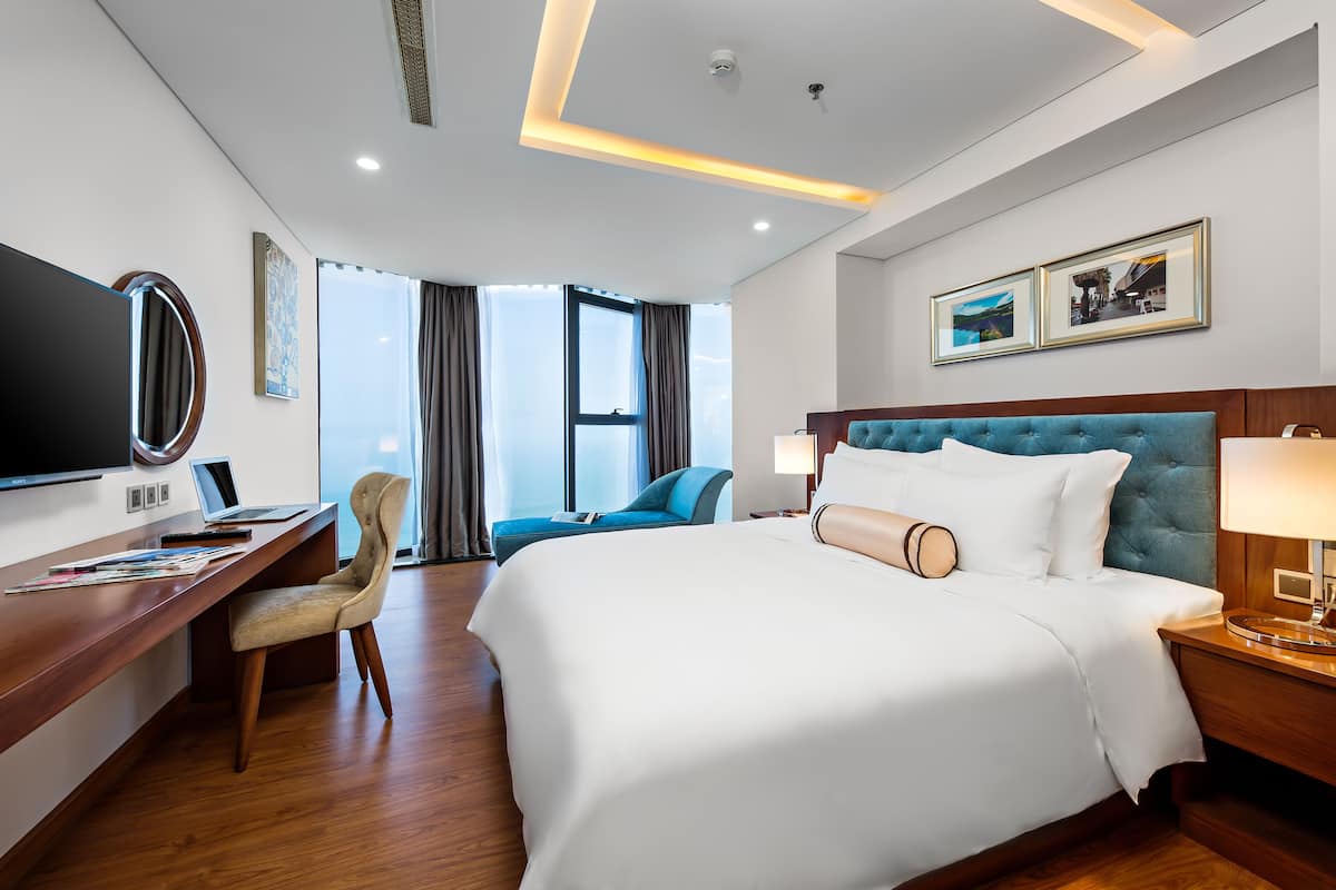 Une chambre d’hôtel avec un grand lit, un bureau avec un ordinateur portable, une chaise et une télévision.