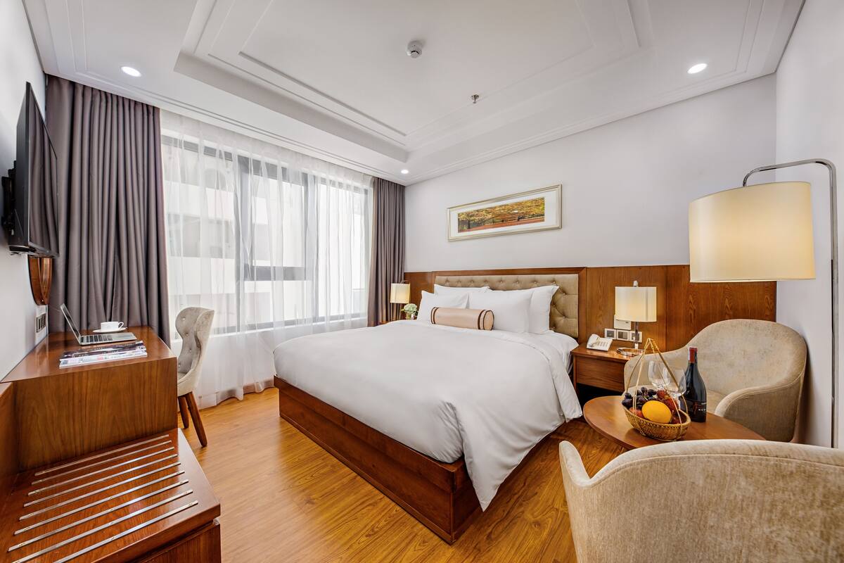 Une chambre d’hôtel avec un grand lit, un bureau avec un ordinateur portable, une télévision, une table de chevet avec une lampe et une chaise.