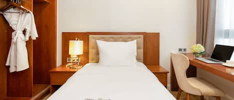 Una habitación de hotel con una cama, un escritorio con una computadora portátil, una silla, un armario y una revista sobre la cama.