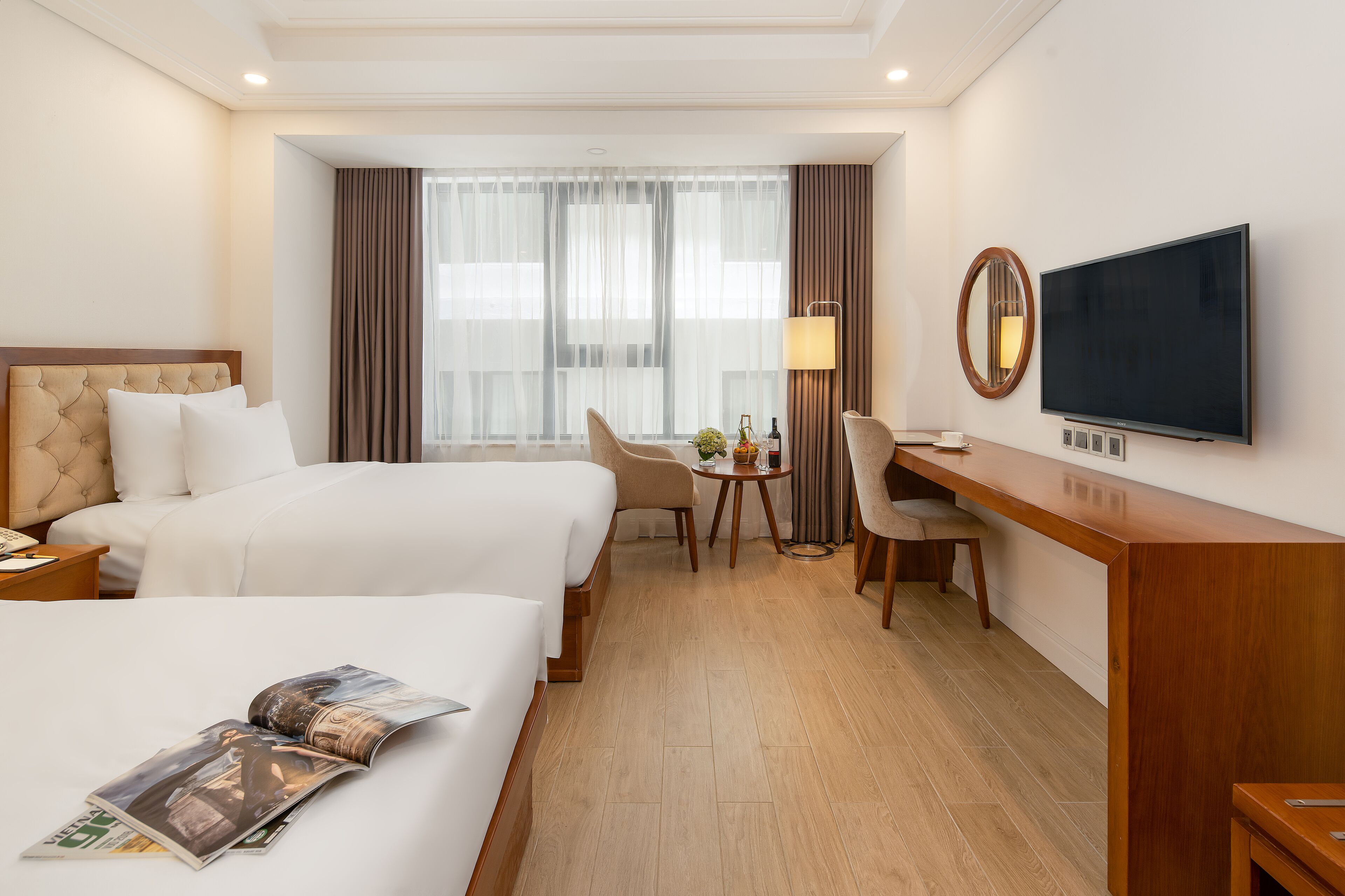A hotel room with two beds, a desk, a TV, and a window with curtains.