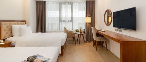 A hotel room with two beds, a desk, a TV, and a window with curtains.