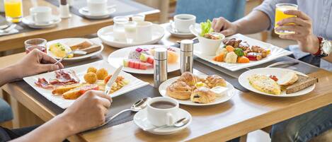 Un desayuno con diferentes platos, como cruasanes, huevos y tostadas, sobre una mesa de madera.