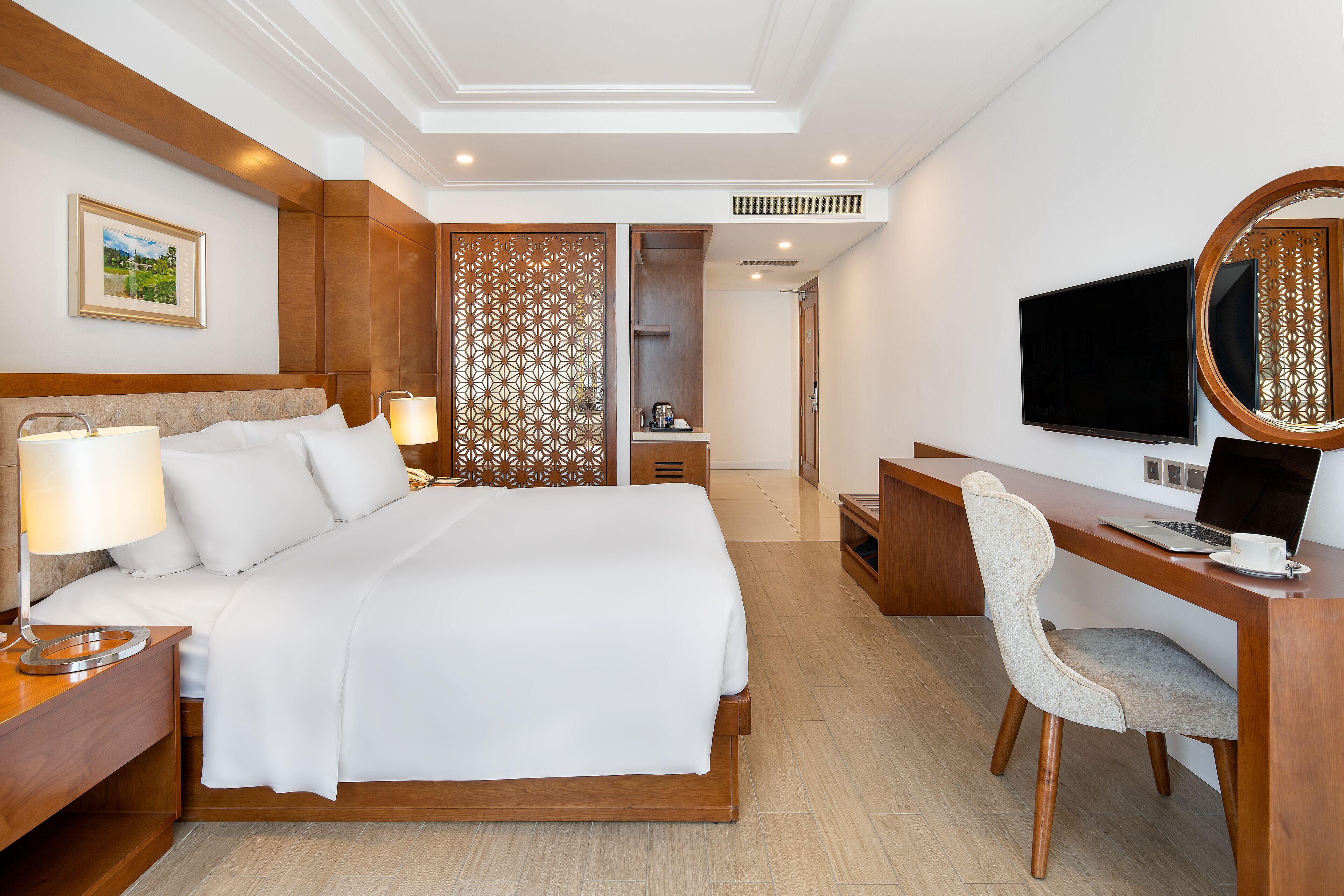 A hotel room with a large bed, bedside lamps, a desk with a laptop, a TV, and a mirror.