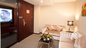 A hotel room with a television on a stand, a sofa, a coffee table with flowers, and a lamp. - YINHAO HOLIDAY HOTEL (Foshan)