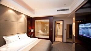 A hotel room with a large bed, a TV, a bathroom with a glass shower, and a door leading to another room. - YINHAO HOLIDAY HOTEL (Foshan)