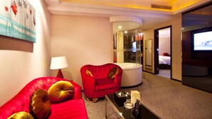 A hotel room with a red sofa, a red armchair, a round coffee table, a TV, and a glass-enclosed bathroom. - YINHAO HOLIDAY HOTEL (Foshan)