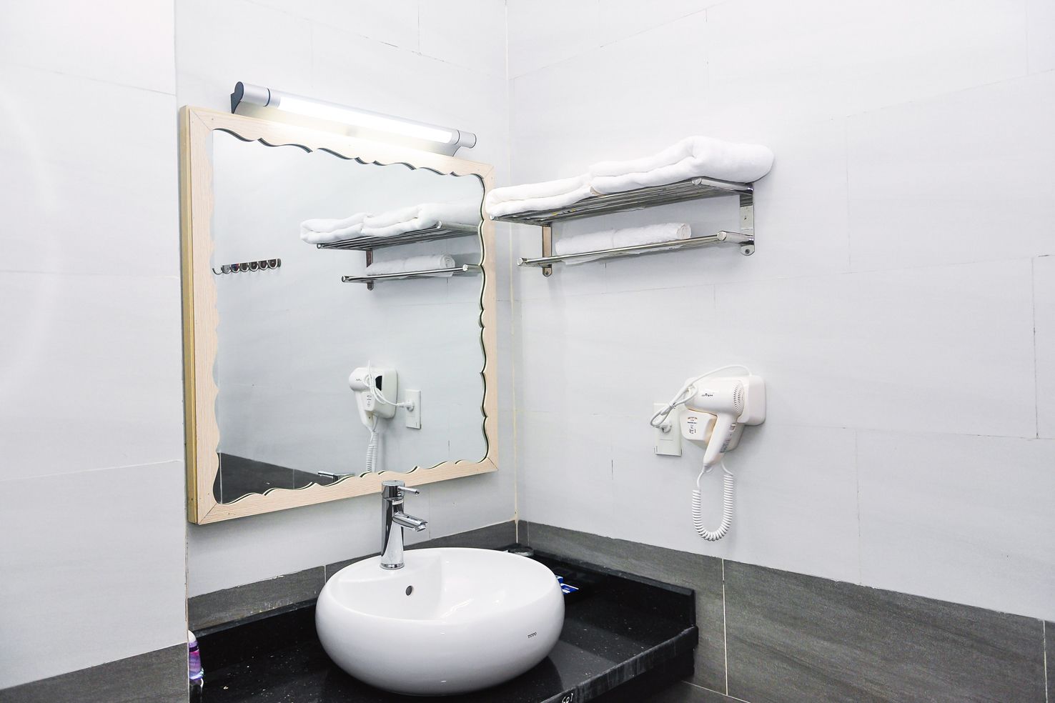 Un baño con un lavabo redondo, un espejo con marco ondulado y dos secadores de pelo montados en la pared.