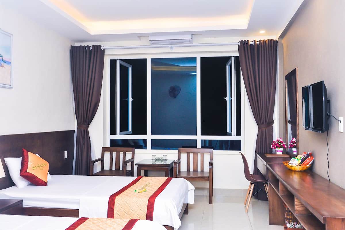 Ein Hotelzimmer mit zwei Betten, einem Schreibtisch, einem Sessel, einem Fernseher und einem Fenster mit Vorhängen.