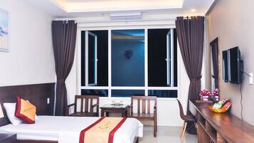 A hotel room with two beds, a desk, a chair, a TV, and a window with curtains.
