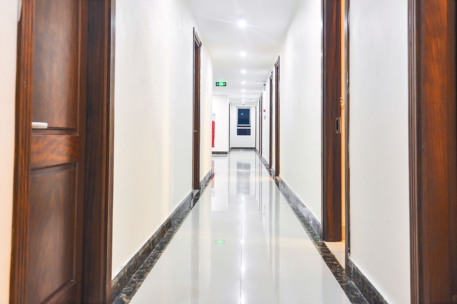 A long, well-lit hallway with wooden doors and a shiny tiled floor.