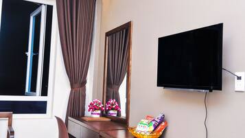 Een hotelkamer met een aan de muur bevestigde televisie, een bureau met een mand met snacks, een spiegel die de gordijnen weerkaatst en een raam met gordijnen.