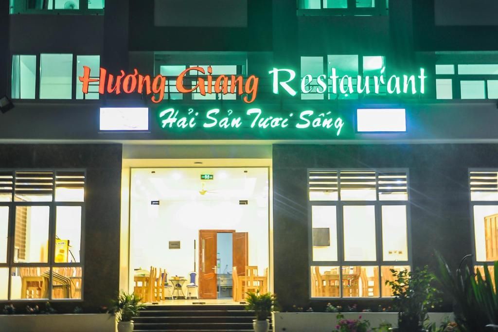 Un restaurante con un letrero de neón, amplios ventanales y una escalera que lleva a la entrada.