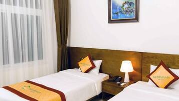 A hotel room with two beds, a painting on the wall, a window with curtains, and a nightstand with a lamp.