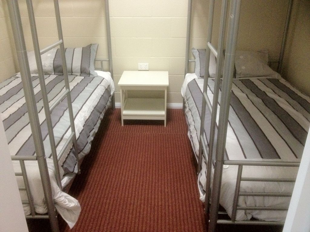 A dormitory room with bunk beds, a small white table, and a red carpeted floor.