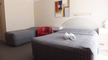A hotel room with a bed, two grey upholstered chairs, a red chair, a white bedside table, and a wall-mounted artwork.