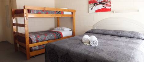 A room with a bunk bed, a single bed, and a painting on the wall.