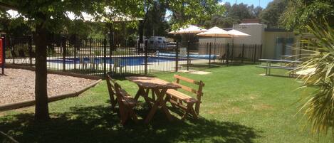 A fenced outdoor area with a pool, picnic tables, and a small building with umbrellas.