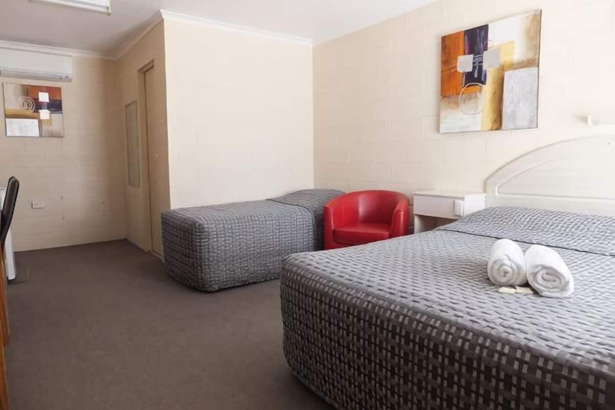 A hotel room with two beds, a red chair, a desk, and a painting on the wall.