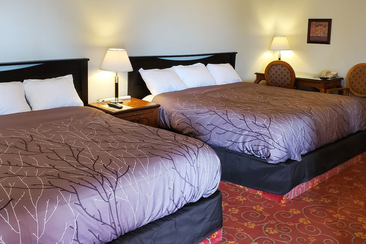 A hotel room with two beds, each with a headboard, bedside lamps, and a nightstand with a phone.