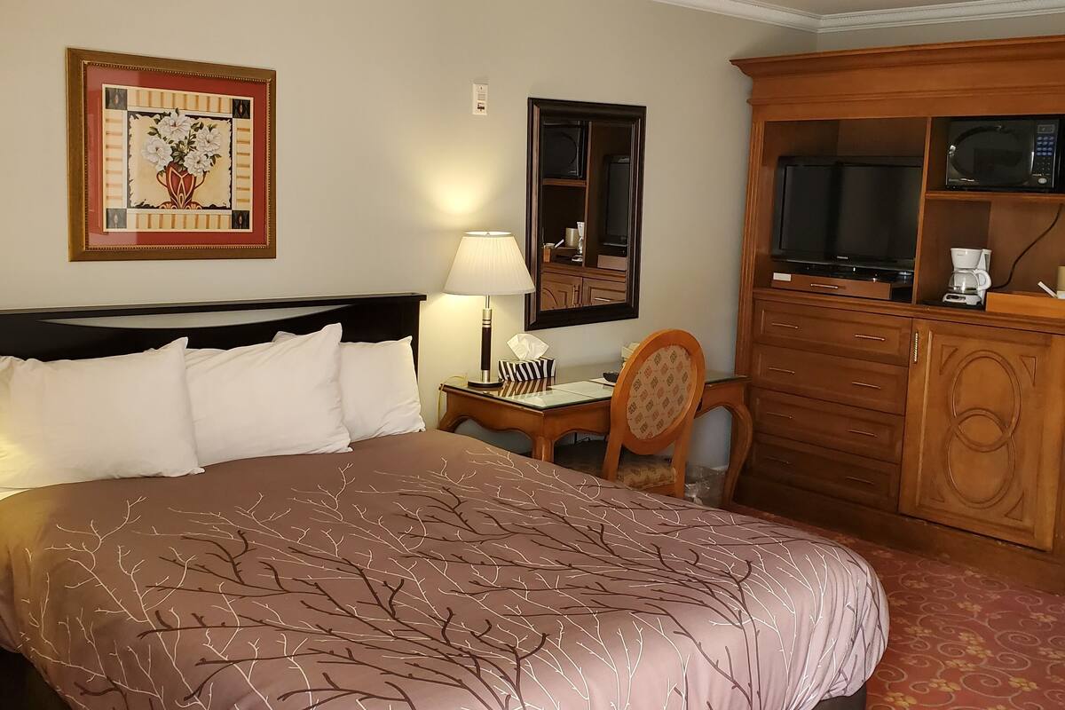 A hotel room with a large bed, a desk with a lamp, a chair, a TV, a microwave, and a cabinet.