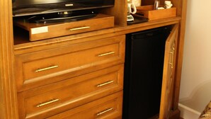 Un mueble de madera con un centro de entretenimiento que incluye un televisor de pantalla plana, un microondas y un refrigerador pequeño.