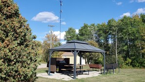 Un pabellón con una parrilla, una mesa de picnic y bancos en un parque.