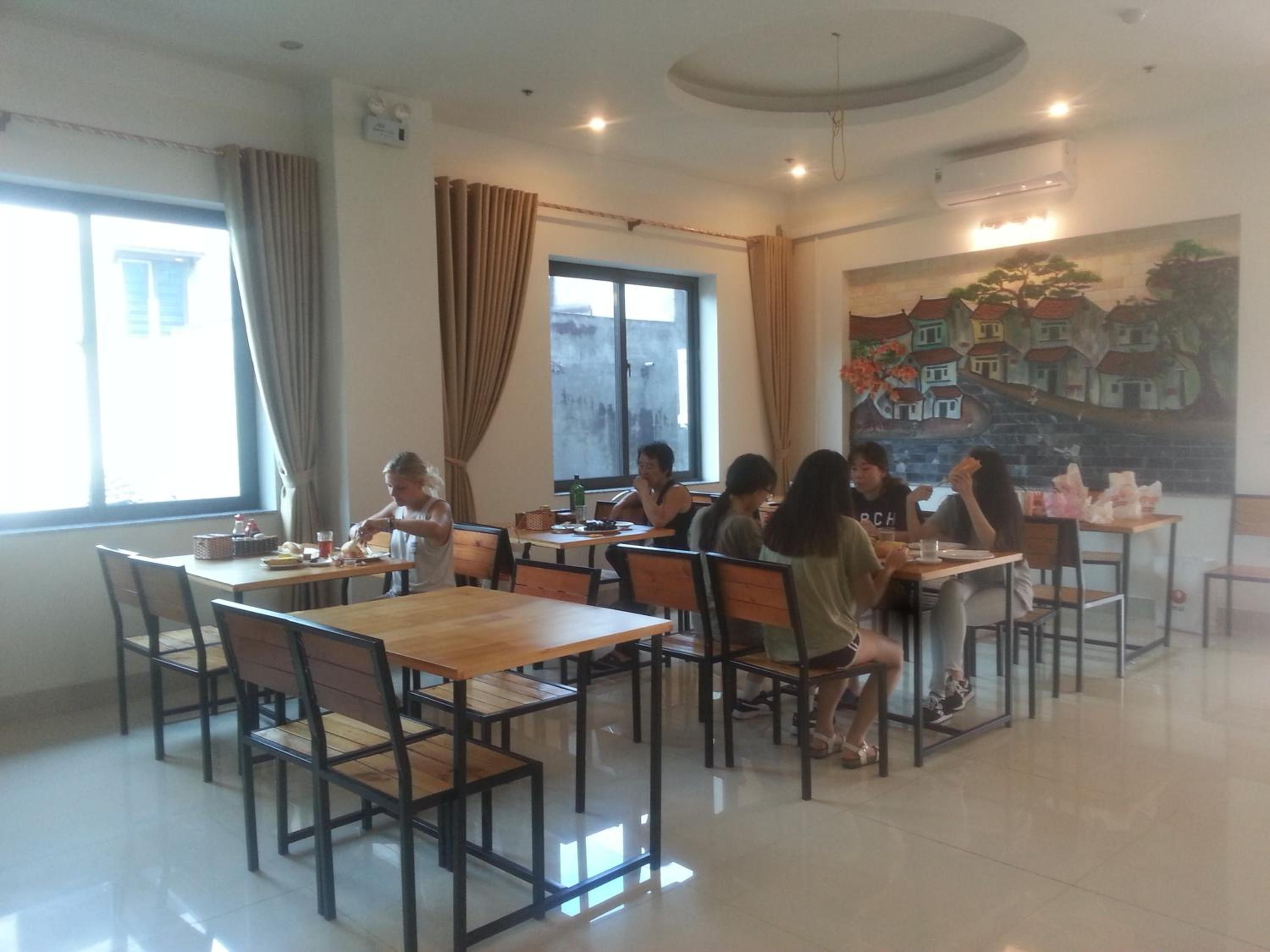 Un comedor con mesas y sillas, un ventanal con cortinas y un mural en la pared.