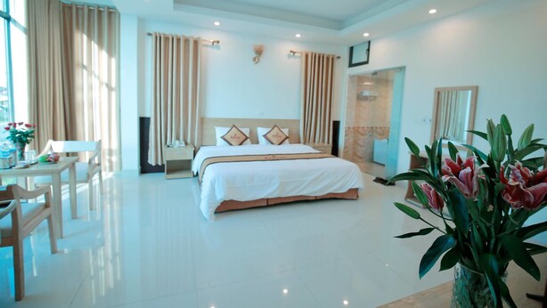 A spacious hotel room with a large bed, a sitting area with a table and chairs, and a vase of flowers. - AVS NOIBAI HOTEL  (Hanoi)