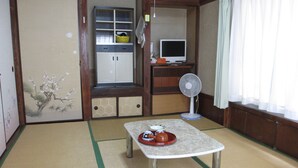 A traditional Japanese room with tatami flooring, a low table with a tea set, a television, and a fan. - YOKOSO Ryokan (Beppu)