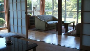A traditional Japanese-style room with tatami flooring, a sofa, a small table, and a fan. - YOKOSO Ryokan (Beppu)