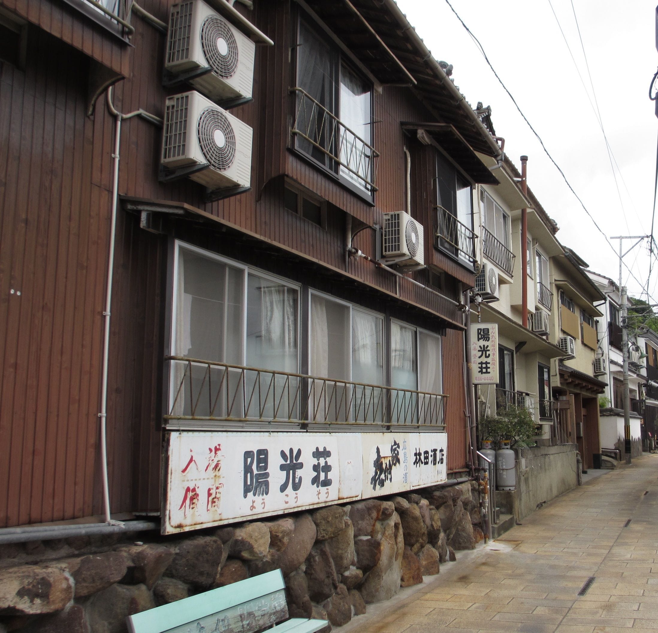 A traditional Japanese building with multiple air conditioning units, large windows, and a stone base.